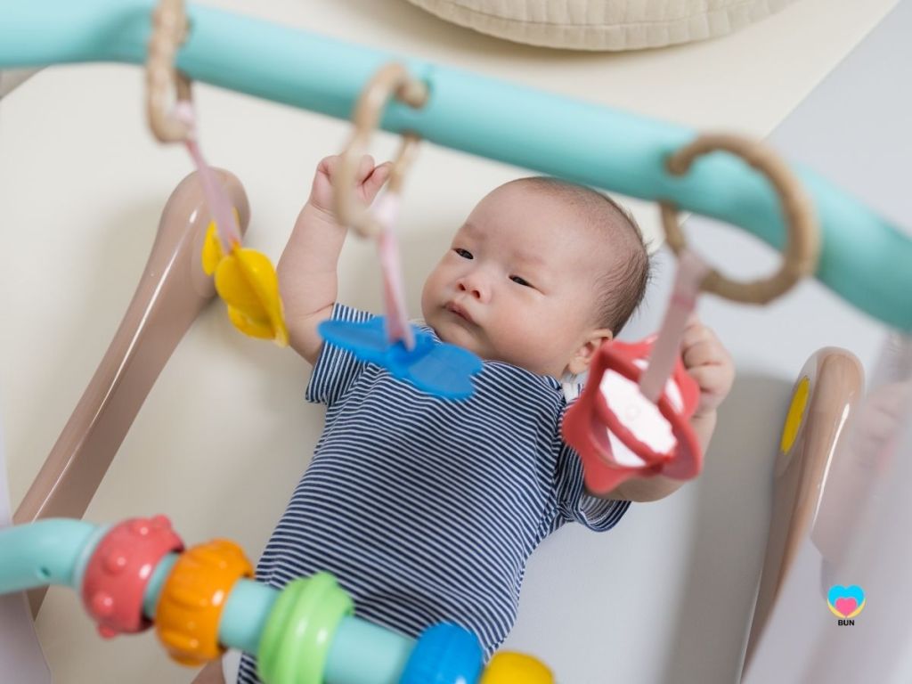 newborn baby playing under mobile on play mat