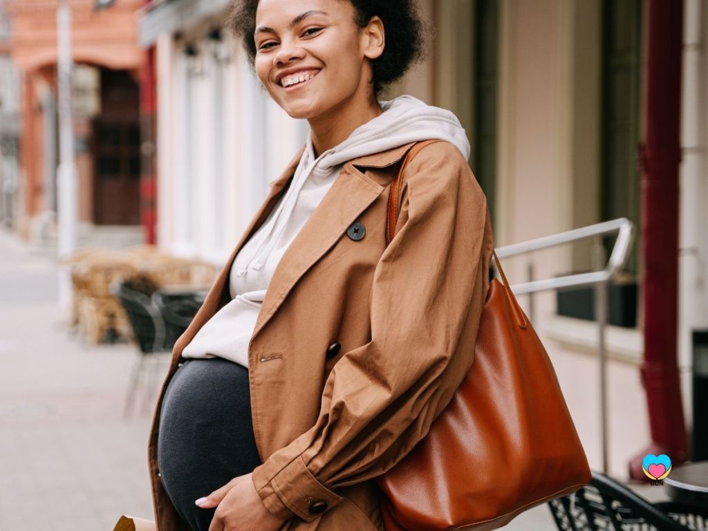 pregnant woman in coat with over shoulder bag smiling and outside